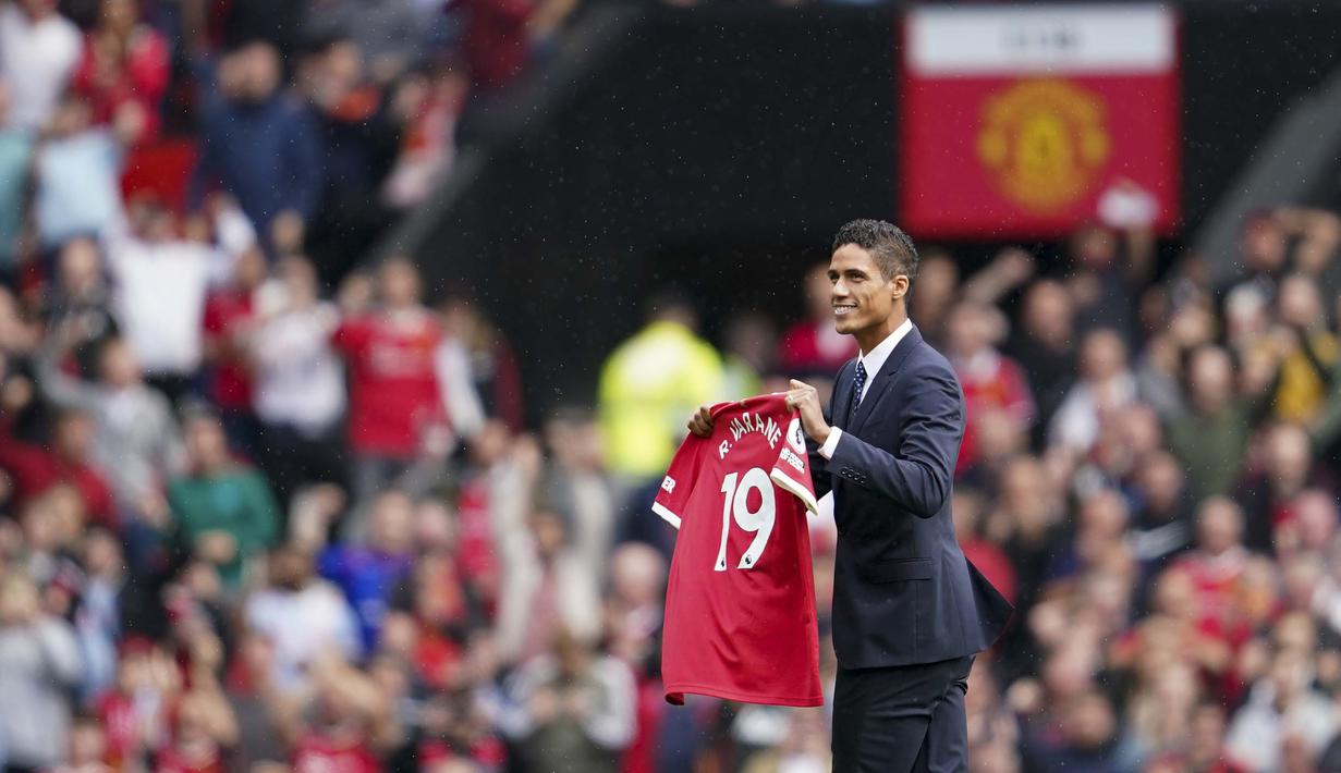 Mengenakan jas berwarna hitam, Raphael Varane menyapa fans di Old Trafford dengan membawa jersey Manchester United. Dia mendapat sambutan meriah dari fans yang memadati Old Trafford. (Foto: AP/Jon Super)