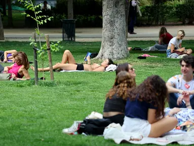 Orang-orang beristirahat di rumput di taman Retiro di Madrid tengah, Spanyol pada 25 April 2023. (AFP/Thomas Coex)