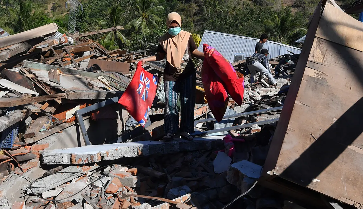 Seorang perempuan membawa bantal melalui puing-puing rumah yang rusak di Menggala, Lombok Utara, Rabu (8/8). Laporan terakhir mengatakan, gempa Lombok telah memakan 105 korban jiwa, dan lebih 70.000 orang kehilangan tempat tinggal. (AFP/ADEK BERRY)