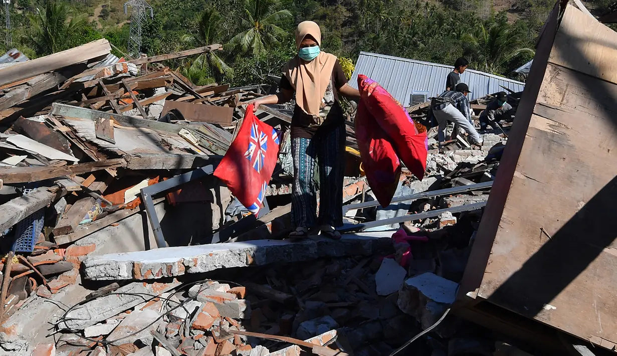 Seorang perempuan membawa bantal melalui puing-puing rumah yang rusak di Menggala, Lombok Utara, Rabu (8/8). Laporan terakhir mengatakan, gempa Lombok telah memakan 105 korban jiwa, dan lebih 70.000 orang kehilangan tempat tinggal. (AFP/ADEK BERRY)