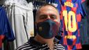 Fans memakai masker berlogo Barcelona di Toko Asesoris Barcelona, Senin (25/5/2020). Di tengah pandemi virus Corona, Barcelona menjual masker dengan harga 18 euro atau sekitar Rp 291 ribu. (AFP/Lluis Gene)