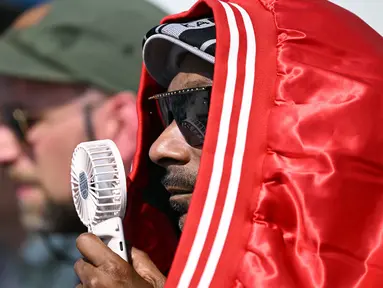 Rapper AS Snoop Dogg mengenakan jaket di kepalanya untuk melindungi dari panas dan memegang kipas portable untuk mendinginkan diri saat ia menonton final skateboard jalanan putra Olimpiade Paris 2024 di La Concorde, Senin (29/7/2024). (Kirill KUDRYAVTSEV / AFP)