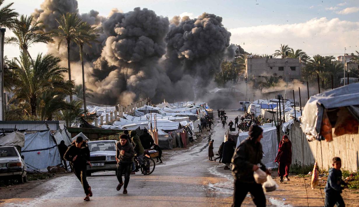 Serangan tersebut memicu kebakaran hebat yang menghanguskan sejumlah tenda pengungsi Palestina di lokasi kejadian. Tampak dalam foto, orang-orang berlarian berlatar kepulan asap hitam setelah serangan udara Israel menghantam sebuah lokasi dekat tenda-tenda penampungan pengungsi Palestina di Deir el-Balah, Jalur Gaza tengah pada 25 Maret 2026. (Eyad Baba/AFP)
