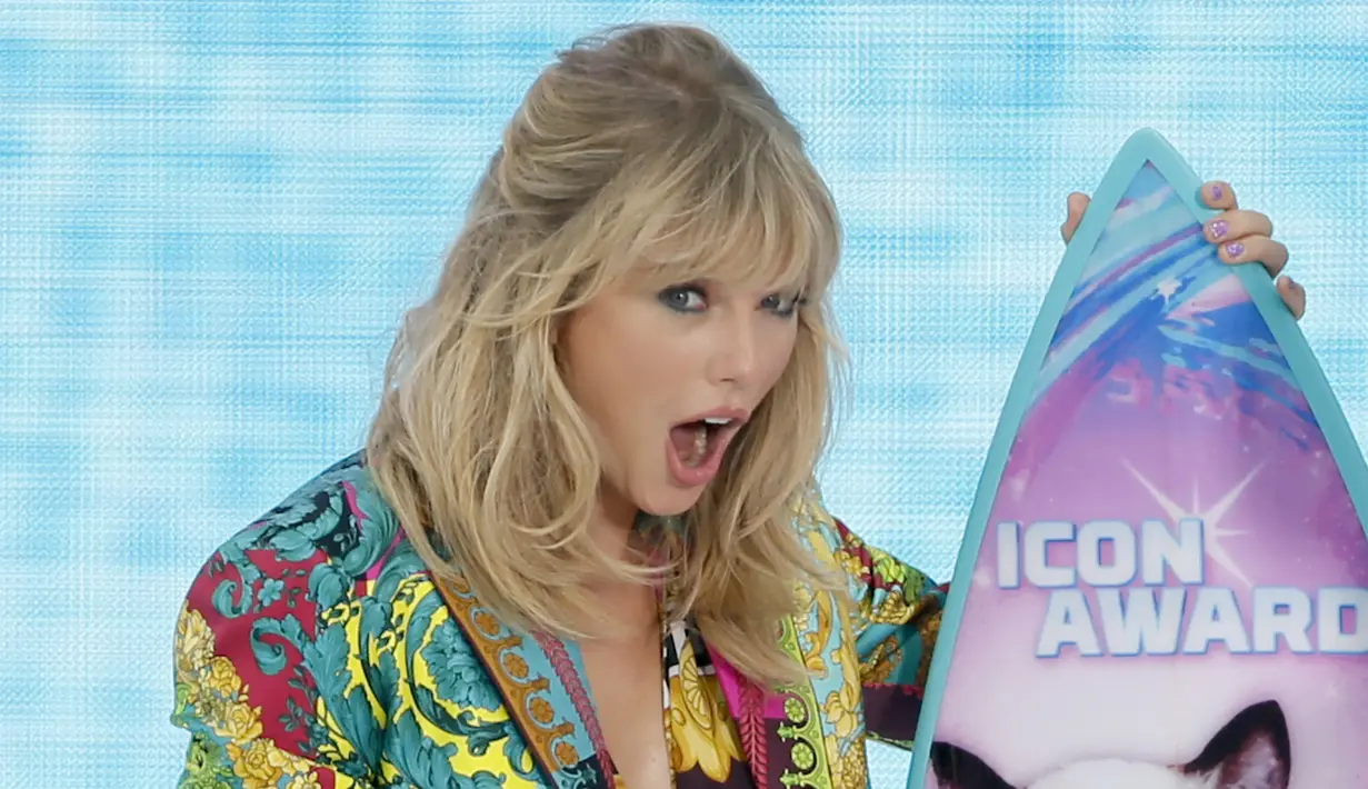 Ekspresi Taylor Swift saat menerima penghargaan Icon Award selama FOX's Teen Choice Awards 2019 di Hermosa Beach, California (11/8/2019). Penyanyi 29 tahun ini tampil cantik mengenakan busana keluaran Versace.  (Rich Fury/Getty Images/AFP)