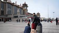 Sepasang suami istri membawa tas menunggu kereta di luar pintu masuk stasiun kereta api Beijing di ibu kota China (7/1/2023). Ketika migrasi tahunan dimulai dengan orang-orang yang kembali ke kampung halaman mereka untuk perayaan Tahun Baru Imlek. (AFP/Wang Zhao)
