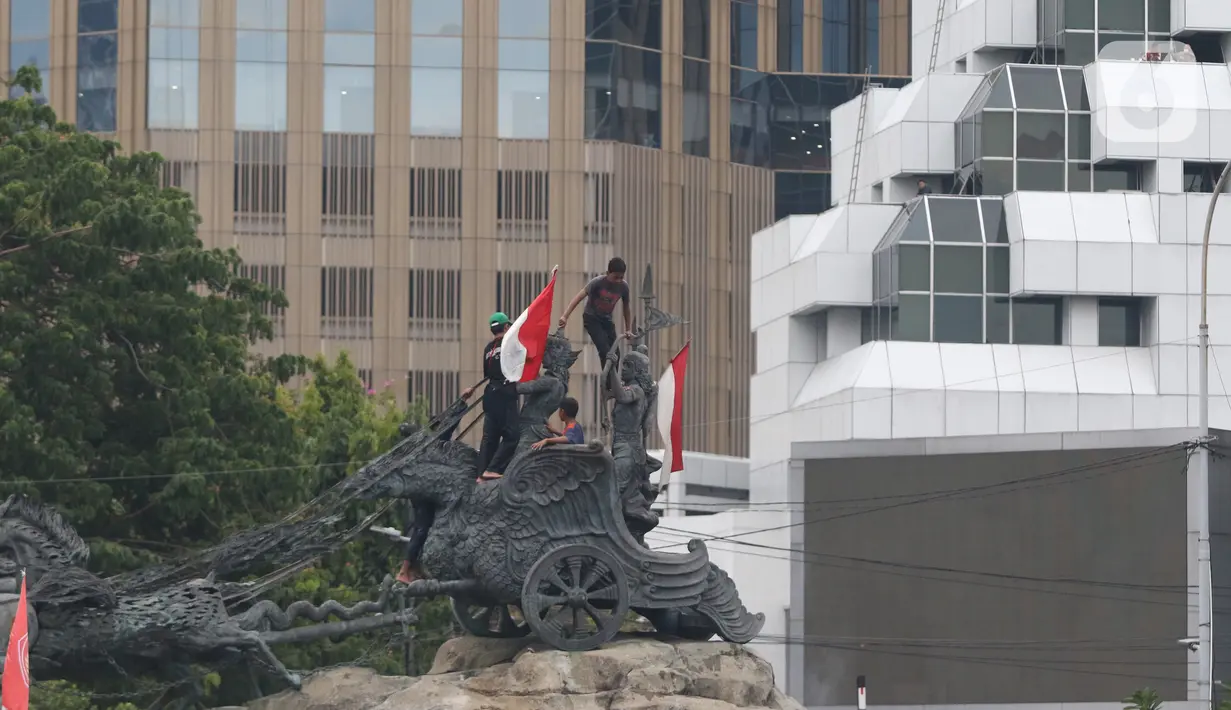 Massa aksi demo tolak omnibus law UU Cipta Kerja naik ke atas patung arjuna wiwaha membawa bendera merah putih di Jalan Medan Merdeka Barat, Jakarta Pusat, Selasa (20/10/2020). Mereka sempat mengibarkan bendera selama kurang lebih lima menit di atas patung. (Liputan6.com/Herman Zakharia)