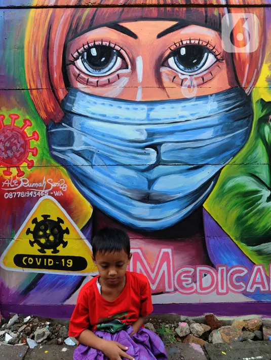 Seorang anak duduk di depan mural bertema COVID-19 di kawasan Tanah Tinggi, Tangerang, Banten, Rabu (20/1/2020). Kegiatan ini dalam rangka mensosialisasikan bahaya penyebaran COVID-19 kepada warga pengguna jalan umum. (merdeka.com/Arie Basuki)
