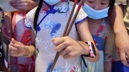 Seorang anak mencoba mengambil kelereng dengan sumpit dalam acara perayaan Festival Pertengahan Musim Gugur di Museum Hainan, Haikou, ibu kota Provinsi Hainan, China selatan (1/10/2020). (Xinhua/Guo Cheng)