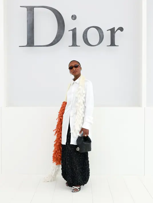 Cynthia Erivo tampil unik dengan kemeja putih dipadu syal bulu oranye-putih di bahu. Rok sequin hitam dan tas kecil hitam jadi pelengkap busana [dok. Dior]