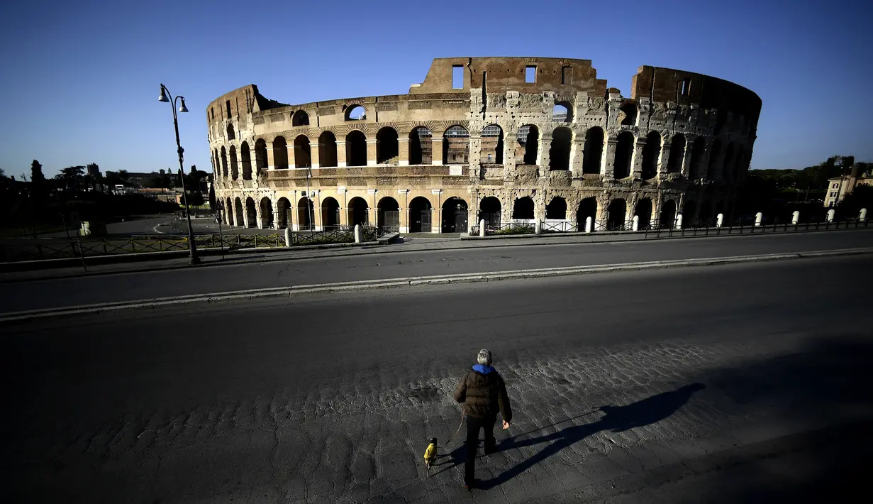 Seorang pria membawa anjingnya jalan-jalan di depan Colosseum, Roma, Italia, 3 April 2020. Menurut Departemen Perlindungan Sipil Italia pada 6 April 2020, jumlah kasus virus corona COVID-19 di negara tersebut menjadi 132.547 infeksi, 16.523 meninggal, dan 22.837 sembuh. (Filippo MONTEFORTE/AFP)