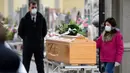 Seorang gadis menyentuh peti mati kerabat yang meninggal saat upacara pemakaman selama masa lockdown untuk menghentikan penyebaran pandemi virus corona COVID-19 di pintu masuk kuburan kecil Bolgare, Lombardy, Italia, Senin (23/3/2020). (Piero CRUCIATTI / AFP)