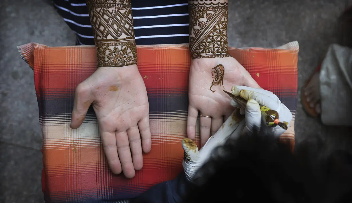 Seorang perempuan mendapatkan desain henna di tangan mereka pada malam festival Karva Chauth di New Delhi, India, Selasa (3/11/2020). Ini adalah festival untuk memulai bulan baru di bulan November di mana para istri akan berpuasa untuk suami-suami mereka. (AP Photo/Manish Swarup)