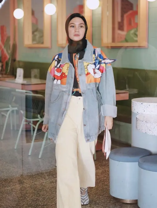 Tantri Namirah juga tampil stylish mengenaka jaket jeans oversize dengan detail kartun. Ia memadukannya dengan kemeja bermotif sebagai inner dan celana putihnya. Padukan dengan kerudung hitam. (@tantrinamirah)