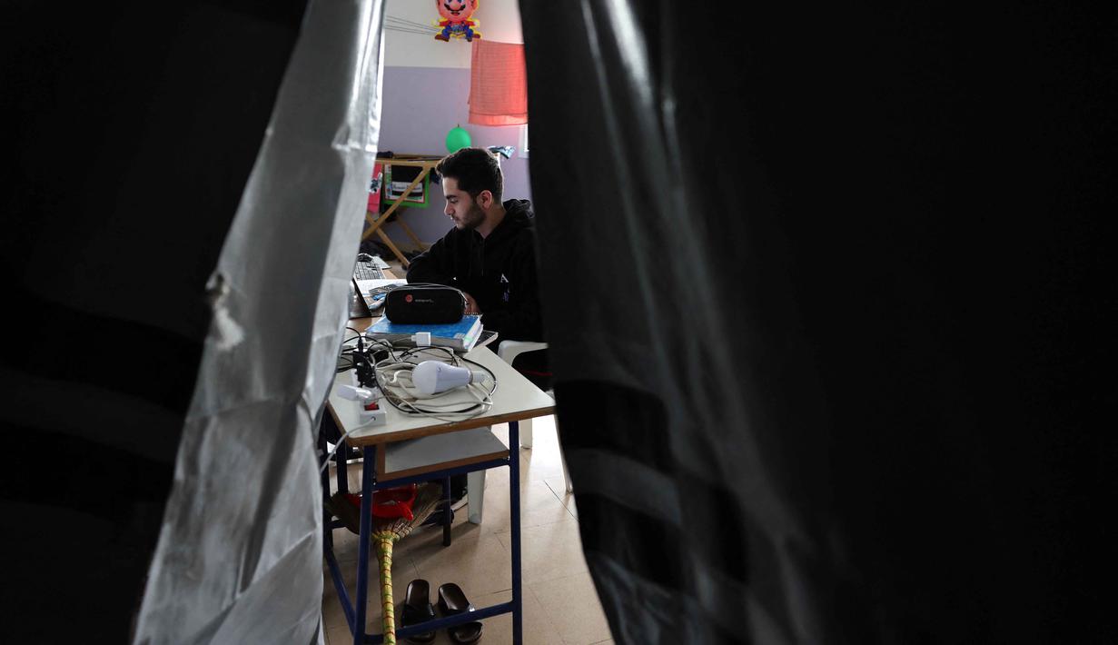 Situasi ini memaksa jutaan anak kehilangan akses pendidikan tatap muka. Tampak dalam foto, seorang pria Lebanon yang mengungsi melanjutkan studinya secara daring di sebuah sekolah negeri yang diubah menjadi tempat penampungan, di kota Dekwaneh, utara Beirut pada Rabu 25 Maret 2026. (Anwar AMRO/AFP)