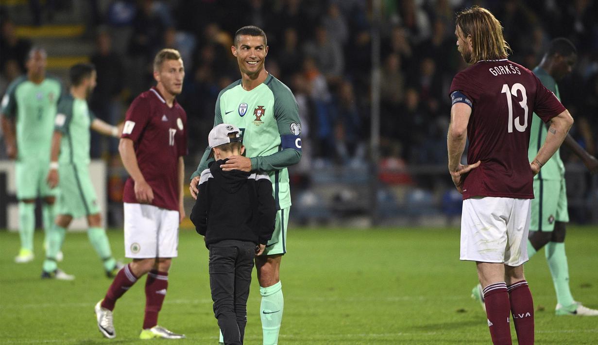 Bintang Portugal, Cristiano Ronaldo, memeluk seorang anak yang menghampirinya usai melawan Latvia pada laga kualifikasi Piala Dunia 2018 di Stadion Skonto, Riga, Jumat (9/6/2017). Latvia kalah 0-3 dari Portugal. (AP/Roman Koksarov)