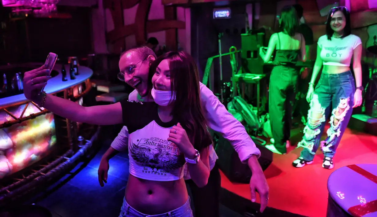 Pengunjung berfoto dengan penari di bar kawasan hiburan Patpong, Bangkok, Thailand, Rabu (1/7/2020). Mulai 1 Juli, bar di Bangkok kembali diizinkan buka setelah pengurangan pembatasan untuk menghentikan penyebaran virus corona COVID-19. (Lillian SUWANRUMPHA/AFP)