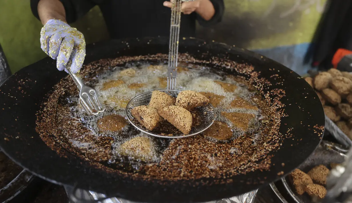 Warga Palestina membuat falafel, makanan yang disukai untuk berbuka puasa, selama bulan suci Ramadhan di pusat kota Hebron di Tepi Barat yang diduduki (9/4/2022). Makanan ini dibuat dari kacang Arab yang digiling dan kemudian dipadatkan dan dibuat bola-bola kecil lalu digoreng. (AFP/Hazem Bader)