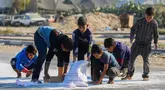Anak laki-laki Palestina mengais tepung dari jalan setelah sebuah tas jatuh dari truk bantuan yang melaju di jalan Salaheddin di Deir el-Balah di Jalur Gaza tengah pada 5 November 2024. (Eyad BABA/AFP)