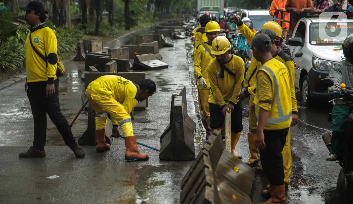 Petugas Sudin Bina Marga merapikan separator busway yang berserakan pascabanjir di Jalan Daan Mogot, Cengkareng, Jakarta, Jumat (3/1/2020). Separator busway tersebut berantakan akibat banjir yang menerjang sejak kemarin. (Liputan6.com/Faizal Fanani)