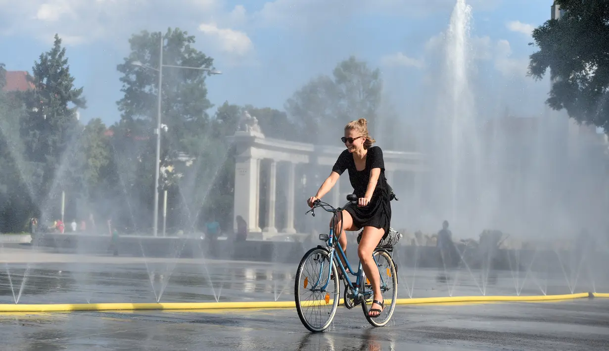 Seorang pesepeda melewati semprotan air di Schwarzenbergplatz di Wina, Austria (28/7/2020). Suhu tertinggi di Wina mencapai angka 37,2 derajat Celsius pada Selasa (28/7). (Xinhua/Guo Chen)