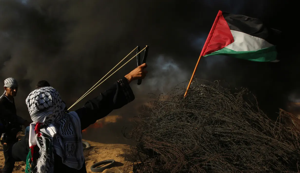 Pengunjuk rasa wanita Palestina menembakkan batu menggunakan ketapel ke arah tentara Israel saat bentrok di Khan Younis, perbatasan Gaza, Jumat (10/8). (AP Photo/Adel Hana)