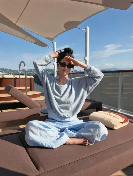 Pada salah satu foto, bintang The Glory itu terlihat duduk bersila di area sun deck mengenakan sweater abu-abu longgar yang dipadukan dengan celana linen biru muda. Rambutnya ditata dalam messy bun sederhana dan dilengkapi kacamata hitam berbingkai ramping. Tanpa aksesori berlebihan, tampilannya justru memancarkan kesan chic khas gaya liburan old money yang sedang digemari. [Dok/@kyo1122].