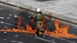 Polisi anti huru-hara melwati jalanan yang terbakar api di Athena, Yunani, (12/11/2015). Para Demonstran juga melakukan aksi mogok kerja selama 24 jam. (REUTERS/Yannis Behrakis)