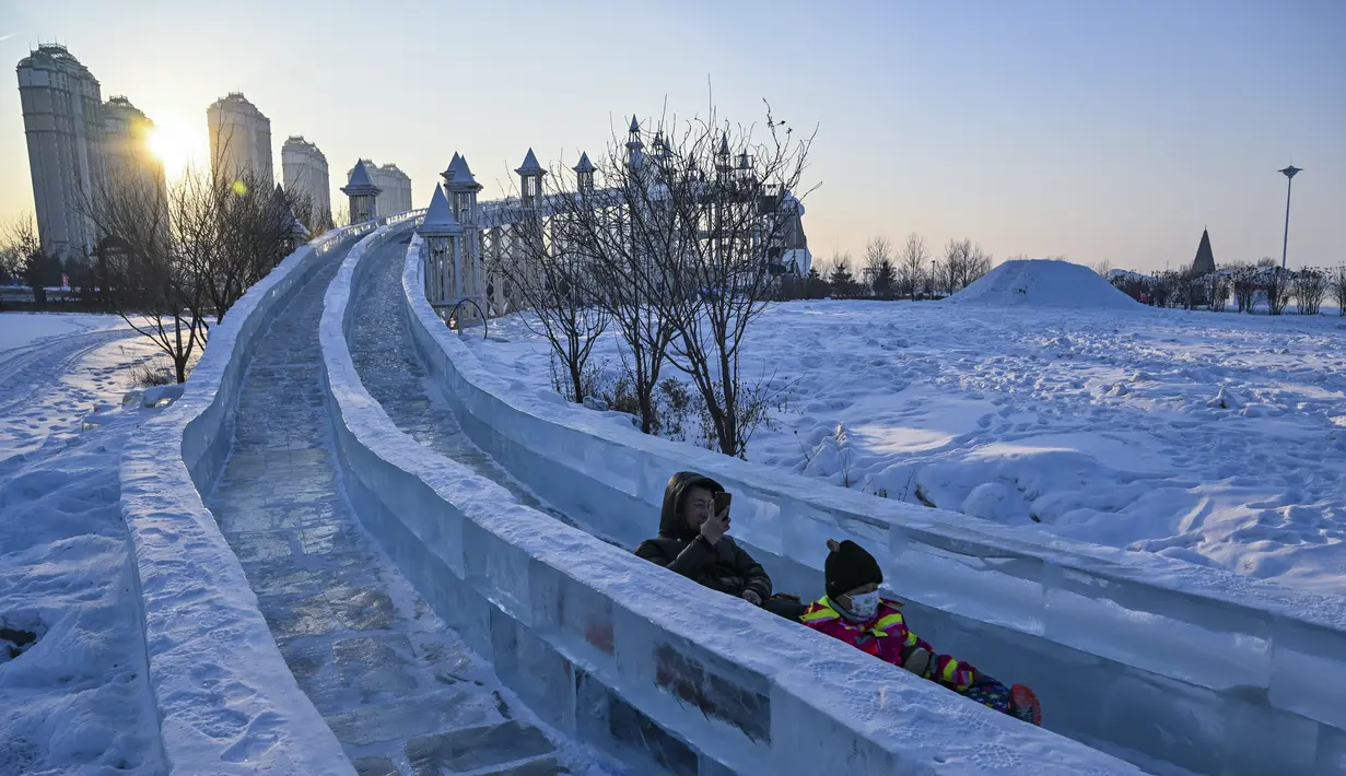 Orang-orang meluncur di seluncuran es di sebuah taman hiburan menjelang Festival Es dan Salju Internasional Harbin Tiongkok ke-39 di Harbin, di provinsi Heilongjiang timur laut China (4/1/2023). (AFP/Hector Retamal)
