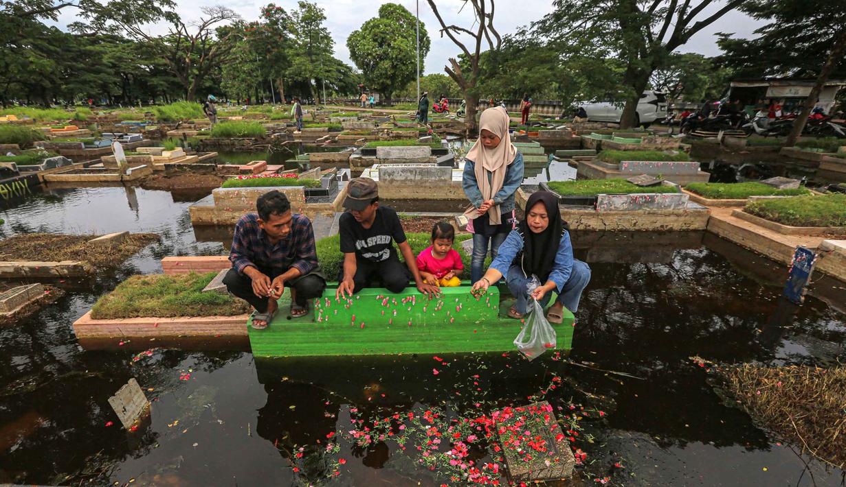 Genangan air yang menutupi area pemakaman membuat akses jalan antar-blok makam menjadi terbatas. Peziarah harus ekstra hati-hati melewati lumpur dan air yang masih menggenang. Tampak dalam foto, warga mengunjungi makam anggota keluarga mereka di Tempat Pemakaman Umum (TPU) Semper, Cilincing, Jakarta Utara pada 15 Februari 2026. (Syinatria RESPATI/AFP)
