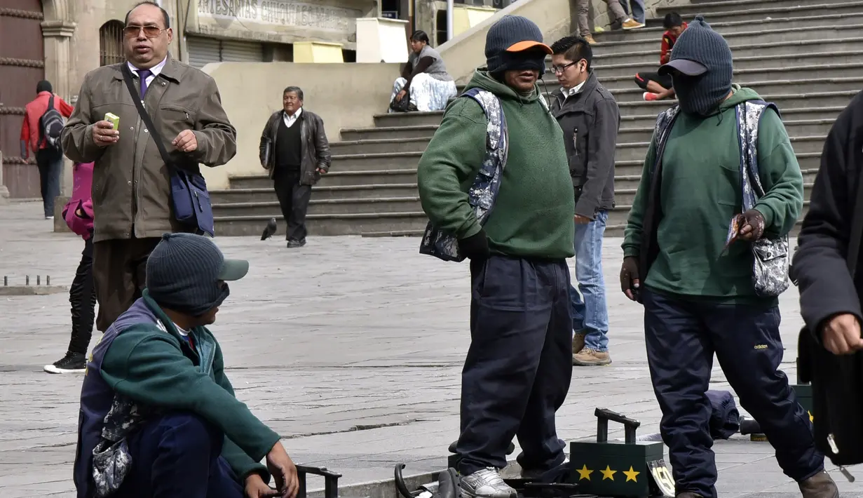 Para tukang semir sepatu bertopeng menunggu pelanggan di kawasan La Paz, Bolivia (29/11). Karena diantara mereka masih ada yang menjalani pendidikan di sekolah dan universitas para tukang semir ini menutup wajahnya. (AFP PHOTO/Aizar Raldes)