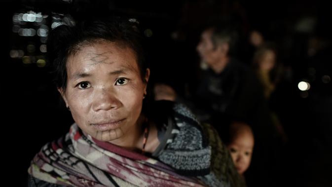 Ku Myo (35), seorang wanita suku Lainong yang bertato menggendong anaknya di rumah mereka di Kota Lahel, Sagaing, Myanmar, 8 Februari 2020. Suku-suku tersebut menjalin kepercayaan animisme mereka dengan tradisi prajurit yang mencakup desain tato mencolok. (Ye Aung THU/AFP)