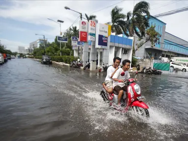 Dua orang remaja mengendarai motor melintasi banjir rob di kawasan Muara Baru, Jakarta, Rabu (6/11). Banjir Rob akibat laut pasang ini, membuat sejumlah aktivitas warga terganggu. Termasuk aktivitas di pasar ikan terhenti. (Liputan6.com/Faizal Fanani)