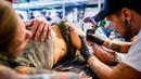 Seorang seniman mentato badan pengunjung wanita dalam acara edisi keempat Montreux Tattoo Convention di Montreux, Swiss  (22/9). Lebih 150 seniman tato dari 22 negara berkumpul dalam acara tersebut. (Valentin Flauraud/Keystone via AP)