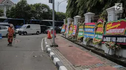 Pasukan oranye membersihkan jalan di dekat karangan bunga bertuliskan ucapan selamat untuk Joko Widodo (Jokowi) dan Ma'ruf Amin di gedung Sekretariat Negara, Jakarta, Senin (22/4). Karangan bunga tersebut ditujukan atas kemenangan Jokowi-Ma'ruf pada Pilpres 2019. (Liputan6.com/Faizal Fanani)