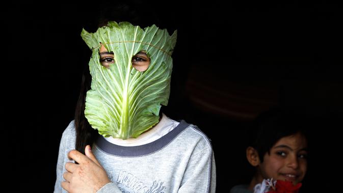 Seorang anak berpose dengan masker dari kubis di tengah wabah pandemi corona (Covid-19) di Beit Lahia di Jalur Gaza utara (16/4/2020). Di tengah pandemi Covid-19, seorang ibu di Jalur Gaza utara mencoba menghibur anak-anaknya dengan masker yang dibuat dari sayuran kubis. (AFP/Mohamed Abed)