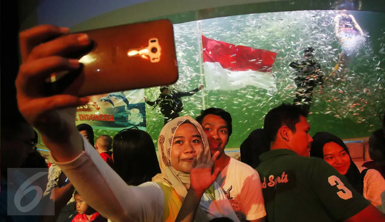 Pengunjung berselfie saat melihat pengibaran bendera Merah Putih di dalam aquarium Ocean Dream Samudra, Ancol, Jakarta (17/8). Taman Impian Jaya Ancol juga mengadakan lomba permainan tradisional, dan panggung hiburan. (Liputan6.com/Immanuel Antonius)