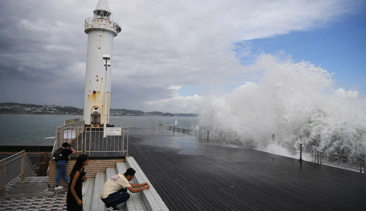 Orang-orang menyaksikan ombak menghantam tepi laut di Pulau Enoshima di pantai Prefektur Kanagawa, barat daya Tokyo (13/8/2019). (AFP Photo/Charly Triballeau)