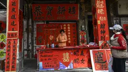 Seorang penjual menjual kuplet musim semi, semacam dekorasi Tahun Baru Imlek, jelang dimulainya Tahun Baru Imlek di sebuah kios di Foshan, Provinsi Guangdong, China, 18 Januari. Angka dua pada kuplet merupakan angka genap yang dikaitkan dengan keberuntungan dalam budaya China. (Giok Gao/AFP)