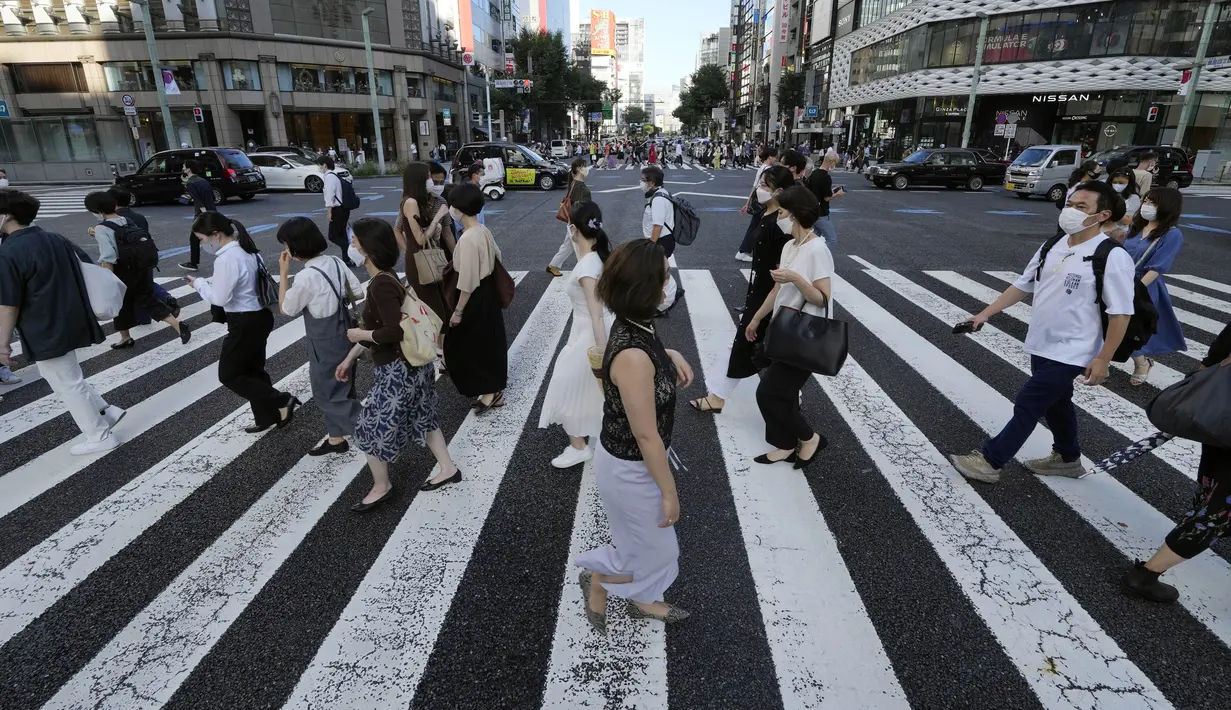 Warga yang mengenakan masker untuk membantu mengekang penyebaran COVID-19 berjalan di sepanjang penyeberangan pejalan kaki di Tokyo, Jepang, Selasa (27/7/2021). Tokyo melaporkan jumlah kasus harian COVID-19 tertinggi beberapa hari setelah Olimpiade dimulai. (AP Photo/Eugene Hoshiko)