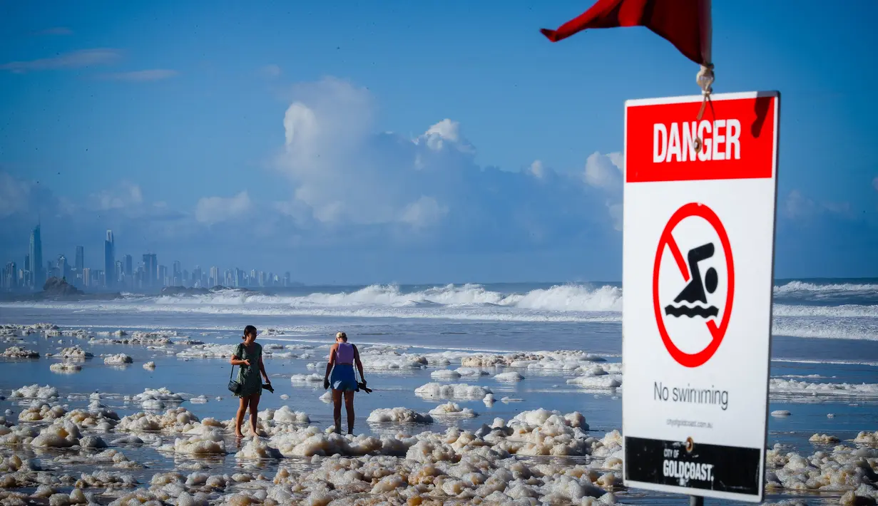 Orang-orang berjalan di antara busa pantai setelah siklon tropis di Currumbin Beach, Gold Coast, Australia pada 15 Desember 2020. Hujan lebat dan angin kencang telah melanda kawasan perbatasan padat penduduk antara New South Wales dan Queensland selama tiga hari. (Photo by Patrick HAMILTON / AFP)