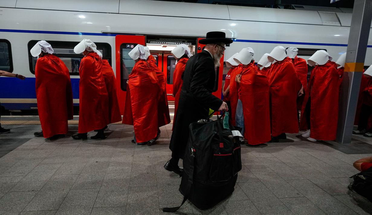 Pengunjuk rasa yang mendukung hak-hak perempuan berpakaian seperti karakter dari serial TV "The Handmaid's Tale" saat melakukan perjalanan untuk memprotes rencana pemerintah baru Perdana Menteri Benjamin Netanyahu untuk merombak sistem peradilan di sebuah stasiun kereta api di Yerusalem, Israel, 1 Maret 2023. Mengacu pada fenomena yang berkembang, harian Inggris The Guardian menggambarkan penampilan para pelayan sebagai salah satu simbol paling kuat dari protes feminis kontemporer. (AP Photo/Ohad Zwigenberg)