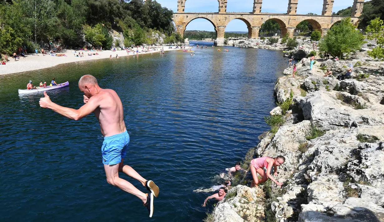 Seorang pria melompat ke sungai di dekat Pont du Gard atau Jembatan Gard di Vers-Pont-du-Gard, Prancis, Rabu (21/8/2019). Pont du Gard merupakan bagian dari saluran air yang panjangnya hampir 50 km. (Pascal GUYOT/AFP)