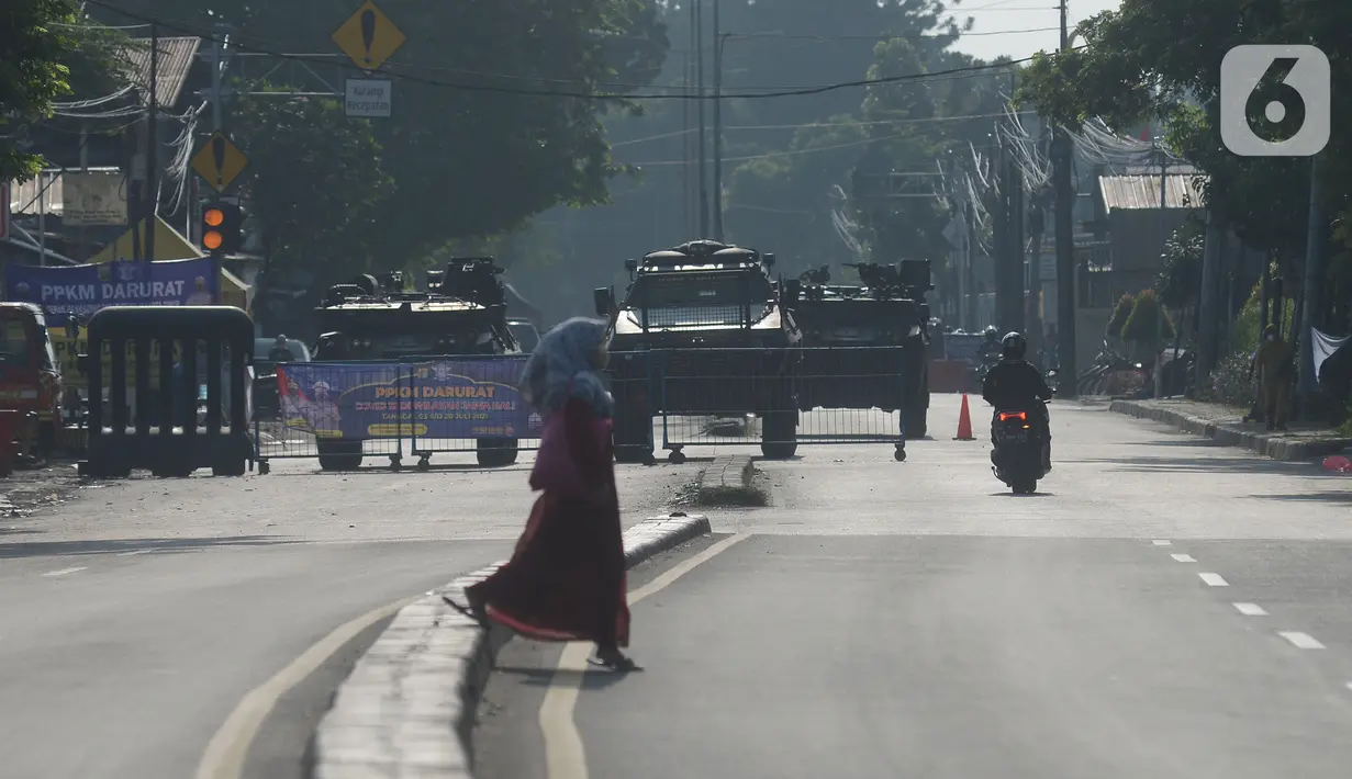 Pengendara melintas dekat barracuda dan panser yang disiagakan di pos penyekatan di Jalan Raya Bogor, Jakarta Timur, Selasa (6/7/2021). Petugas Gabungan Polri dan TNI menyiapkan kendaraan taktis untuk membantu penyekatan selama PPKM Darurat Jawa - Bali. (merdeka.com/Imam Buhori)