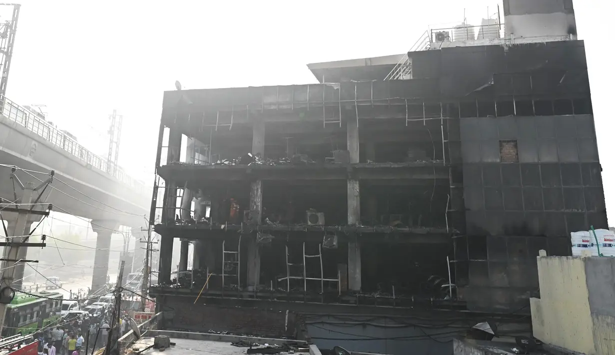 <p>Orang-orang menonton dari jalan ketika anggota Pasukan Tanggap Bencana Nasional dan petugas pemadam kebakaran memeriksa sebuah gedung komersial sehari setelah kebakaran terjadi di New Delhi, India, Sabtu (14/5/2022). Kebakaran yang melanda gedung perkantoran empat lantai di Delhi, pada Jumat 13 Mei 2022, menewaskan sedikitnya 27 orang dan melukai sedikitnya 12 orang, kata layanan darurat. (Sajjad HUSSAIN / AFP)</p>