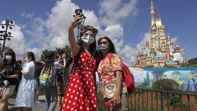 Para pengunjung yang mengenakan masker untuk mencegah penyebaran COVID-19 berswafoto di Disneyland Hong Kong, Kamis (18/6/2020). Disneyland Hong Kong kembali beroperasi pada 18 Juni 2020 dengan menerapkan sejumlah protokol kesehatan baru. (AP Photo/Kin Cheung)