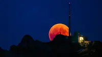 Bulan tampak berwarna merah darah saat terjadinya fenomena gerhana bulan total  di Luzern, Swiss, Jumat (27/7). Gerhana bulan yang terlama pada abad ini dapat disaksikan di seluruh dunia dengan mata telanjang. (Christian Merz/Keystone via AP)