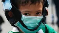 Seorang anak laki-laki mengenakan masker saat dijemput orang tuanya di Bangkok (30/1). Kementerian Kesehatan Thailand memberi peringatan kepada warga dan turis untuk menghindari kegiatan di ruang terbuka dan mengenakan masker. (AP Photo/Sakchai Lalit)