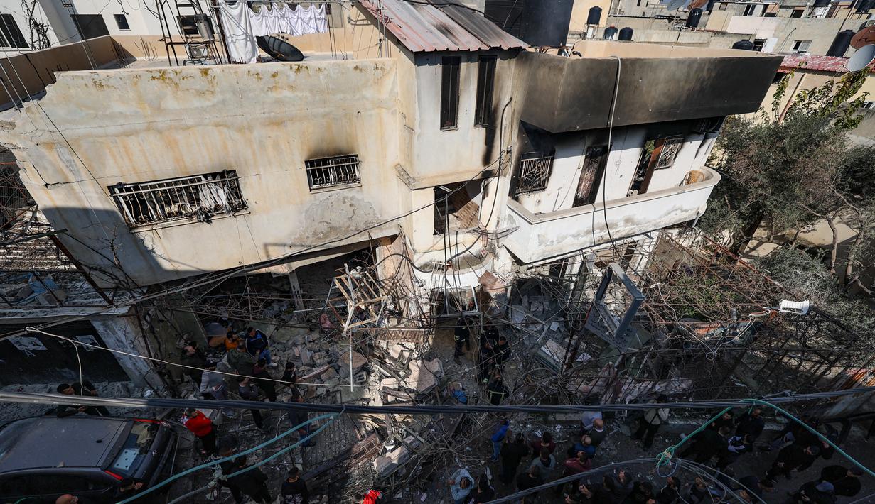 Orang-orang berkumpul di sekitar bangunan yang dirusak dan dibakar oleh pasukan Israel selama penggerebekan di kamp pengungsi Jenin Tepi Barat, pada 26 Januari 2023. Tentara Israel menggunakan gas air mata di dalam rumah sakit dan menolak berkomentar ketika ditanya oleh AFP tentang tuduhan gas air mata. (AFP/Jaafar Ashtiyeh)