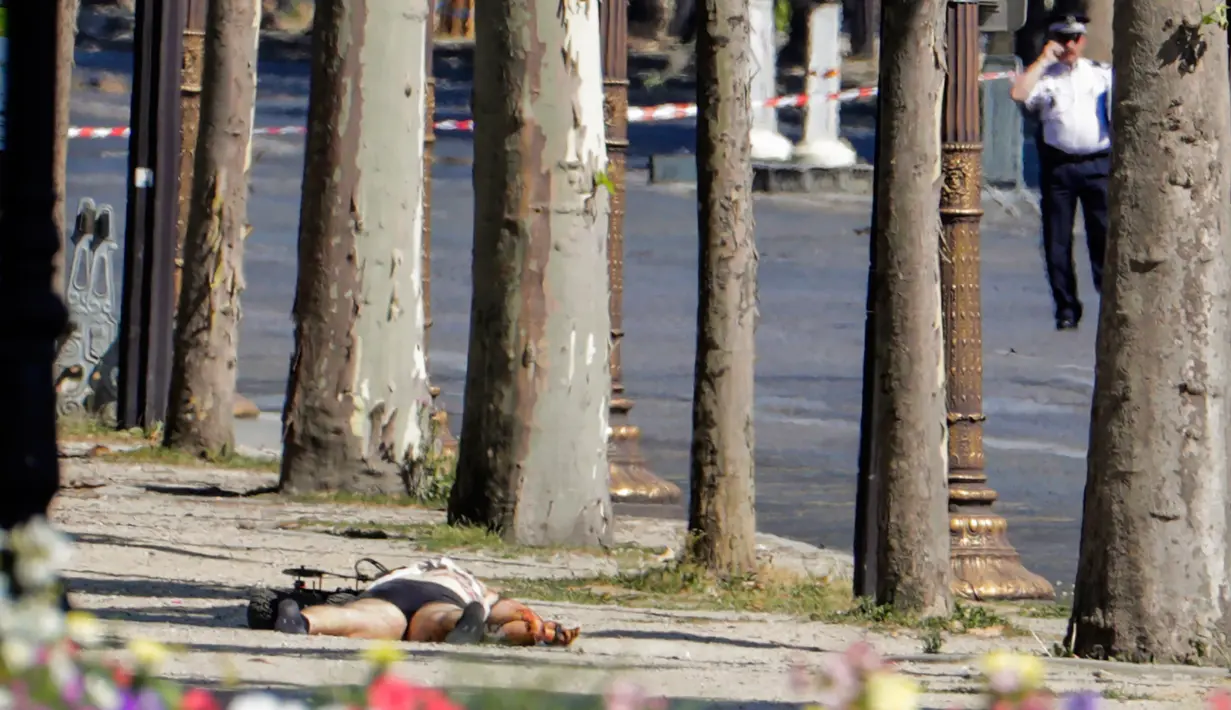 Alat pengontrol jarak jauh (kiri) memeriksa jasad seorang pria usai serangan terhadap van polisi di jalan Champs Elysees, Paris, Senin (19/6). Pria itu sengaja menabrakkan mobilnya yang berisi bahan peledak ke van milik polisi. (Thomas SAMSON / AFP)
