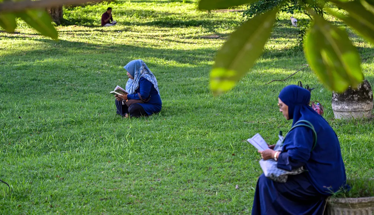 Diketahui, pada dua dekade silam, tepatnya pada 26 Desember 2004, Aceh luluh lantak dihantam gelombang tsunami. Tampak dalam foto, para wanita membaca Al-Quran sambil berdoa untuk kerabat mereka yang meninggal dunia dalam peristiwa gempa dan tsunami Aceh pada 2004 lalu di sebuah kuburan massal di Siron, pada 26 Desember 2025. (CHAIDEER MAHYUDDIN/AFP)